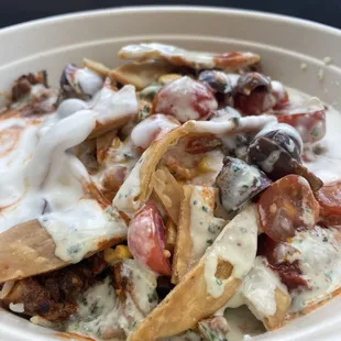 Grain bowl with saffron basmati rice, harissa chicken, veggies, pita crisps, tzatziki, harissa, garlic, and lemon herb tahini.