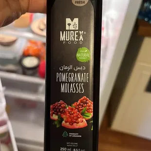a hand holding a bottle of purex pomegranate molassses