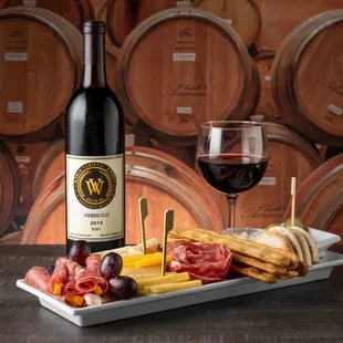 a platter of meat, cheese, and grapes with a glass of wine