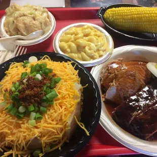 Two lunch meat special with two sides (corn and Mac n cheese) with banana pudding and a side of a baked potato