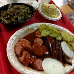 Two meat dinner plate with link sausage and sliced beef. Sides  of green beans and potato salad.