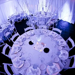 Formal table settings include white resin chairs, satin linens and napkins, chargers, flatware, elegant wine glasses and plates.
