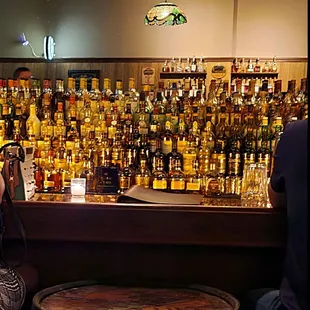 a woman taking a picture of a bar full of liquor bottles