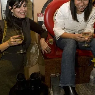 two women sitting on a red chair holding wine glasses