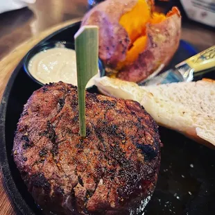 a steak on a black plate with a side of bread