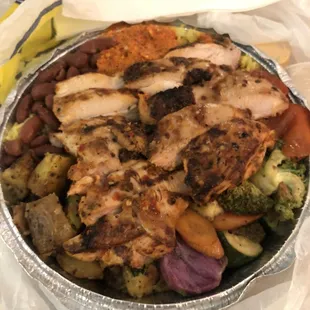 Chicken bowl with rice, veggies, beans, potatoes, and spicy sauce.