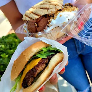 a woman holding a hamburger and a sandwich