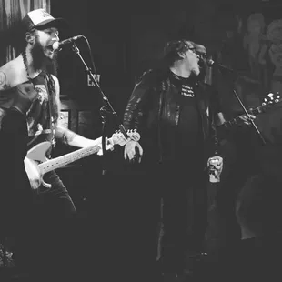 a black and white photo of two men playing guitar
