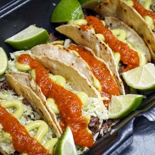 a tray of tacos with sauce and lime wedges