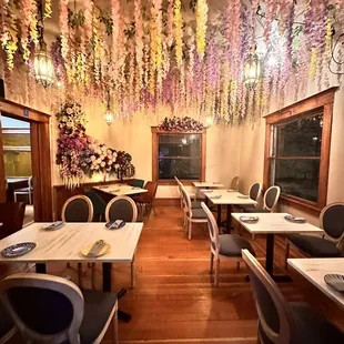 tables and chairs with flowers hanging from the ceiling