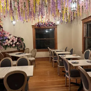 tables and chairs with flowers hanging from the ceiling