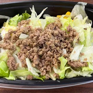 Bowl with white rice and "steak". It also has black beans, corn, iceberg lettuce, salsa, and avocado.