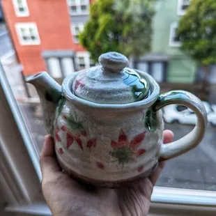 a hand holding a teapot in front of a window