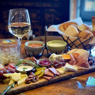 a wooden board with cheese, bread, grapes, and breadsticks