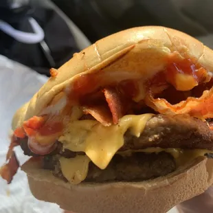 a hand holding a sandwich with bacon and cheese
