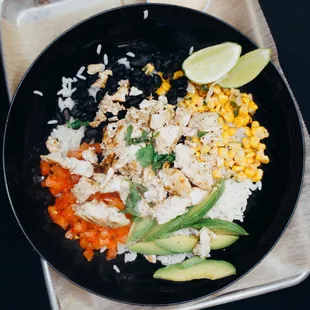 a black plate with rice, chicken, corn, avocado, and black beans