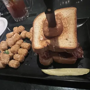 a sandwich and tater tots on a black plate