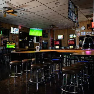 a bar with stools and televisions