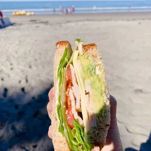 a person holding a sandwich on the beach