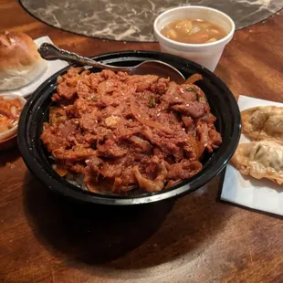 Spicy Pork Bowl with dumplings and kimchi, a side of curry vegetables, and a soft bread roll