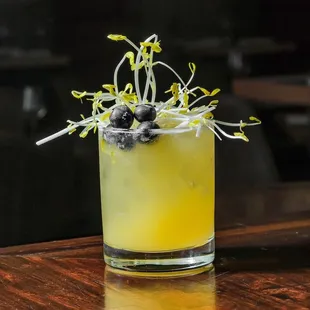 a yellow cocktail with blueberries on the rim