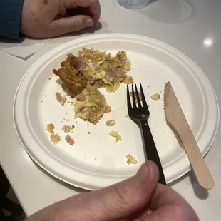 Quiche Lorraine remains on paper plate with plastic fork and wood knife.