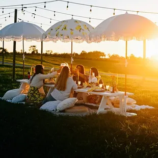 a group of people sitting at a picnic table under umbrellas