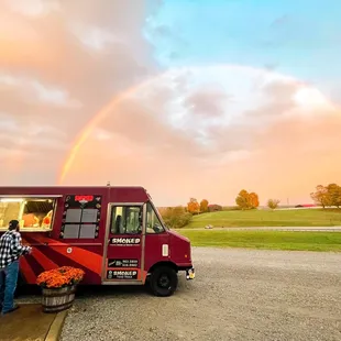 a man standing in front of a food truck with a rainbow in the background