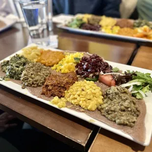 Checher Vegan Deluxe - an assortment of vegetable stews, include peas, lentils, collard greens, carrots, and more, served atop injera
