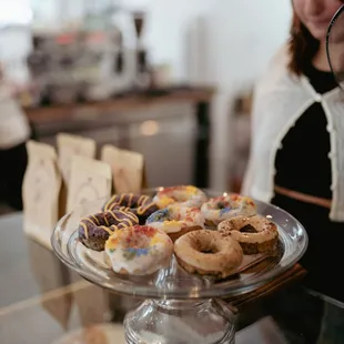 a woman standing behind a counter with donuts