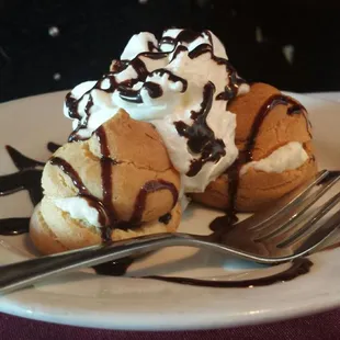 Three baby cream puffs with chocolate sauce.