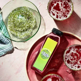 a glass of chichacha on a pink plate next to a bottle of chichachacha