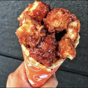 a hand holding a cone of fried chicken