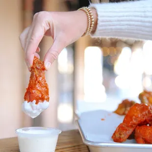 a person dipping sauce onto a plate of chicken wings