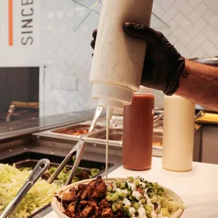 a person pouring dressing into a bowl