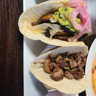 Vegan taco and carne asada taco. Vegan taco has black beans,  mushrooms,  onions,  and guacamole