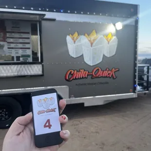 a person holding a cell phone in front of a food truck