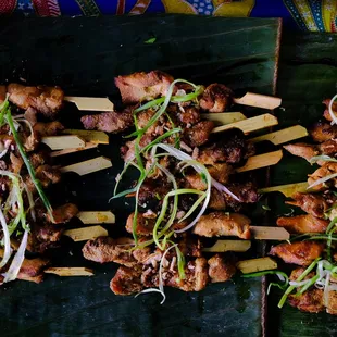 several skewered meats on a banana leaf