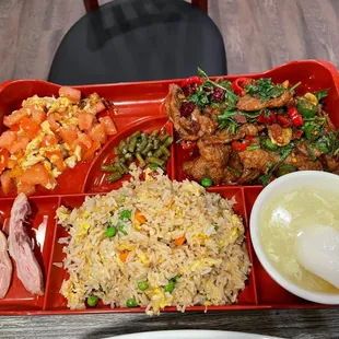 a red tray with rice, chicken, vegetables, and soup