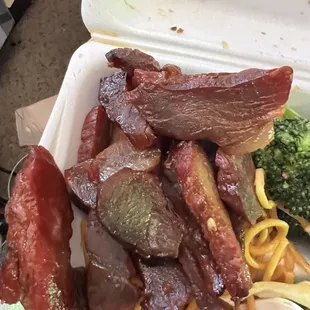 a takeout container with noodles, meat, and broccoli