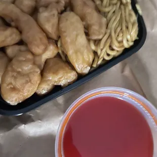 a tray of noodles, chicken, and a cup of tea