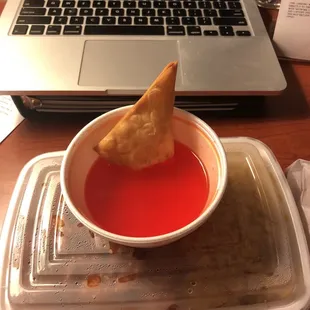 a bowl of soup and a small cracker in front of a laptop