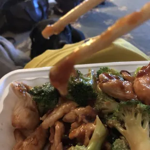 a plate of broccoli and chicken with chopsticks