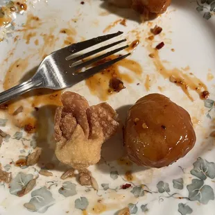 Tiny baby bite size cream cheese wonton in comparison to the giant, very breaded sesame chicken nugget and large fork.