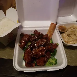 Sesame chicken with broccoli, steamed rice, steamed dumplings and an eggroll.