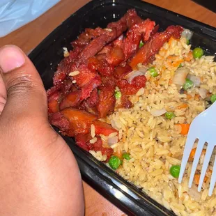 a hand holding a fork and a plate of rice with meat and vegetables