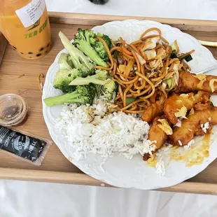 Orange chicken with little pieces of a fresh slice of orange on top, broccoli in garlic sauce, white rice, and veggie lo neon noodles.