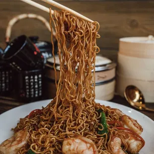 a person holding chopsticks over a plate of noodles