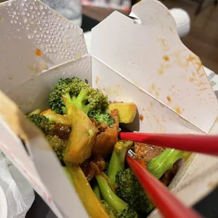 a take out box of food with chopsticks