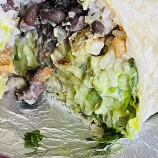 Burrito consisting of lettuce, white cilantro rice, chicken, guacamole, picó de gayo, black beans, and cheese.